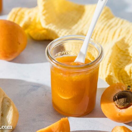 Leckere Aprikosenmarmelade aus nur 3 Zutaten in einem Weckglas. Darin steckt ein weißer Löffel.